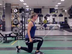 Kvinna utför utfallssteg med vikt i ett gym. Hon håller en hantel i ena handen och har ett ben framåt och ett bakåt.