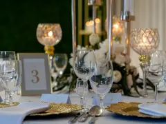 Elegancko nakryty stół weselny z kieliszkami, złotymi talerzami i świecami. Czy warto personalizować każdy element wesela od serwetek po etykiety? Tak!