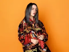 Billie Eilish teraz w kolorowej kurtce z nadrukiem na pomarańczowym tle.