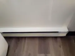 Dylatacja posadzki przy ścianie, biała listwa przypodłogowa z czarną szczeliną, drewniana podłoga.