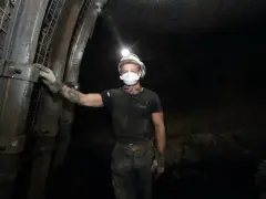 Górnik w kasku z lampką na głowie i masce ochronnej stoi w kopalni. To trudny, ale ważny zawód.
