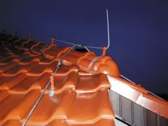 System piorunochronu na dachu z brązowej dachówki, pokazujący, jak działa piorunochron, odprowadzając energię burzy.