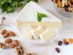 Queso brie en cuña y trozos, decorado con menta. Alrededor hay almendras, nueces y frutos secos. Ideal para quienes buscan información sobre queso brie calorias.