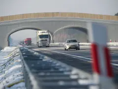 Autostrada A2 z mostem nad jezdnią, jadące samochody i ciężarówki w zimowej scenerii.