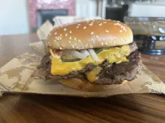 Podwójny cheeseburger z roztopionym serem, piklami i cebulą na bułce z sezamem.