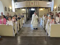 Uroczyste odnowienie przyrzeczeń chrzcielnych w kościele. Dzieci z zapalonymi świecami siedzą w ławkach, a ksiądz błogosławi zgromadzonych.