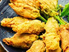 Fiori di zucca ripieni dorati e croccanti, serviti su un piatto blu scuro.
