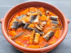 Un sabroso all i pebre en cazuela de barro, con trozos de anguila y patatas en una salsa rojiza.
