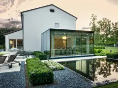 Ampliamento casa con estensione esterna in vetro, con piscina e arredi da giardino.