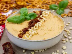 Aksamitny hummus z suszonymi pomidorami i orzeszkami pinii, udekorowany listkami bazylii. Idealny do chrupiących precelków.