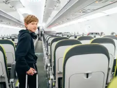 Chłopiec z słuchawkami na szyi i walizką w ręku stoi w przejściu samolotu. Od ilu lat można latać samemu? Ryanair pozwala na samodzielne podróże od 12 roku życia.