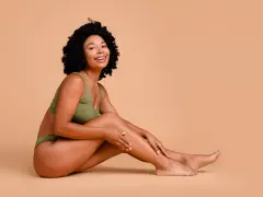Femme souriante en sous-vêtements verts, caressant sa jambe. Elle partage ses secrets pour comment avoir des pieds doux.