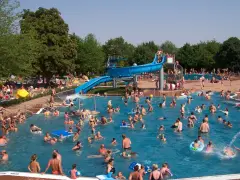 Ein belebtes Freibad in Goslar mit vielen Menschen, die im Wasser planschen und die blaue Wasserrutsche genießen.