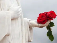 Kamienna dłoń trzyma bukiet trzech czerwonych róż.