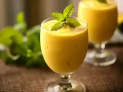 Orzeźwiający koktajl z mango, udekorowany listkami mięty, w szklance na nóżce. W tle drugi taki sam napój.