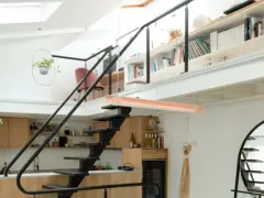 Aménagement mezzanine ouverte avec escalier métallique, cuisine en bois, étagères remplies de livres et plantes suspendues.