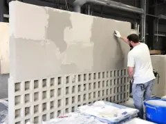 Un homme applique de l'enduit sur un mur en parpaing ajouré, créant une texture unique.