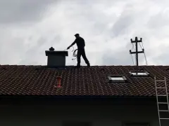 Kominiarz na dachu sprawdza komin. Zastanawiasz się, ile kosztuje przegląd kominiarski?