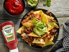 Nachos con carne, guacamole y salsa en un plato negro, con botella de Heinz y cuencos de salsa.