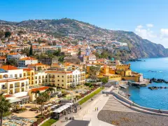 Widok na Funchal, stolicę Madery, z kolorowymi budynkami wznoszącymi się na zboczu góry, otoczonymi błękitnym oceanem.