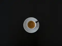 Czarna filiżanka espresso na białym spodeczku na ciemnym tle. Może symbolizować początek walki z objawami odstawienia kofeiny.