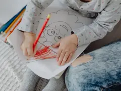 Mały rysunek dziecka z kredkami. Dziecko koloruje czerwoną kredką.