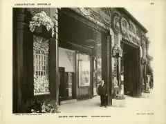 Façade de galerie de boutiques, style art déco, avec ornements floraux et motifs circulaires. Un homme en costume se tient sur le trottoir.