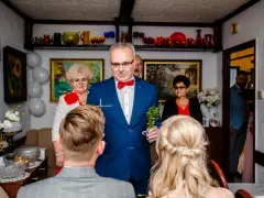 Mężczyzna w niebieskiej marynarce dokonuje tradycyjne błogosławieństwo, trzymając krzyż i gałązkę.