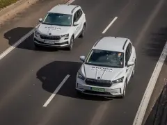 Dwa białe samochody Skoda Auto Szkoła jadą po drodze, gdzie obowiązuje ruch lewostronny.