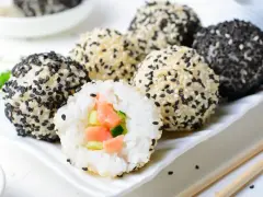 Kuliste sushi, obtoczone białym i czarnym sezamem, z widocznym wnętrzem z łososiem i ogórkiem. Prawdziwa uczta dla miłośników kuchni japońskiej.