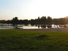 Drewniane pomosty na spokojnym jeziorze starogrodzkim, z piaszczystą plażą i zieloną trawą w tle.