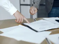 Dwie osoby przy biurku analizują dokumenty. Jedna wskazuje palcem na tekst, druga trzyma długopis, gotowa do podpisania. To może być moment, gdy omawiają, co to jest list żelazny.
