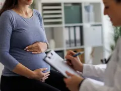 Visita medica: una donna incinta tiene la pancia mentre il medico annota sul foglio, forse il tracciato delle contrazioni preparatorie.
