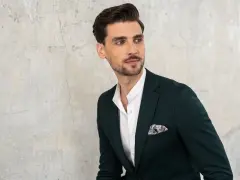 Elegancki mężczyzna w ciemnozielonej marynarce i białej koszuli z kołnierzykiem stójka, z poszetką w kieszeni.
