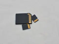 Trzy czarne karty pamięci: jedna większa, przypominająca kartę SD, oraz dwie mniejsze, typu microSD. Złote styki widoczne na każdej karcie.