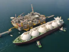 Praca na statku LNG: potężna jednostka z kopułami ładunkowymi przy platformie wydobywczej, holowniki asystują.