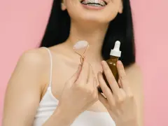 Uśmiechnięta kobieta z aparatem ortodontycznym trzyma jadeitowy roller i serum. Rozpoczyna wprowadzanie retinolu do swojej rutyny pielęgnacyjnej.