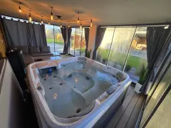 Relaks w jacuzzi pod ciepłym światłem lamp w przeszklonym tarasie zimowym. Obok wygodna sofa i stolik.