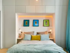Idee salvaspazio camera da letto piccola: letto con testiera contenitore, quadri colorati e tende turchesi creano un ambiente accogliente.