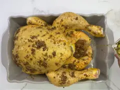 Un pollo al ast, sazonado y listo para hornear, recibe un chorrito de aceite para una cocción perfecta.