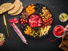 Planche apéro généreuse : charcuterie, fruits secs, olives, tomates, fromage, cornichons et pain. Une belle idée pour un moment convivial.