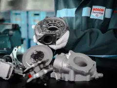 Mechanik w rękawiczkach prezentuje części turbosprężarki, sugerując domowe ustawienie sztangi turbiny.