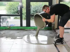 Mann gießt ausgleichsmasse auf fliesen. Der Boden wird nivelliert.