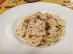 Pici cacio e pepe, un classico piatto romano, servito in un piatto bianco, con abbondante pepe nero macinato.