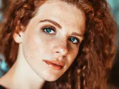 Primo piano di una ragazza con lentiggini e capelli rossi, con un trucco naturale che esalta la sua bellezza.