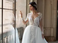 Panna młoda w sukni ślubnej z koronką i trenem, z ozdobną fryzurą w stylu bollywood, patrzy przez okno.