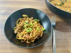 Pyszny makaron wok z kawałkami wołowiny i brokułami, posypany szczypiorkiem. Danie prezentuje się apetycznie w czarnej misce.