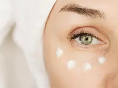 Augenpartie mit feinen Linien, die auf erste Falten unter den Augen mit 20 hindeuten. Cremepunkte unter dem Auge für Pflege.