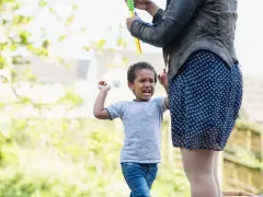 Ein 3-jähriges Kind hat einen Wutanfall, während eine Person Seifenblasen macht.