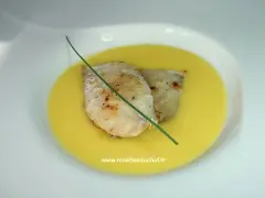 Deux filets de poisson poêlés reposent dans une onctueuse sauce à l'orange, décorés d'une tige de ciboulette.